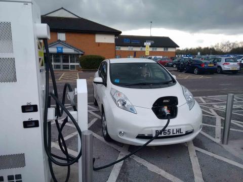 A white Nissan Leaf attached to an Electric Highway CHAdeMo rapid charger at a motorway service station