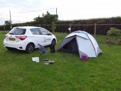 A white Toyota Yaris parked in a camping field next to a white 3-person tent