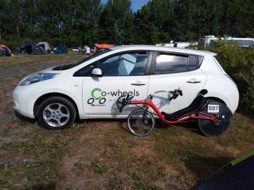 Optima Baron recumbent bicycle leaning against a white Nissan Leaf with a Co-Wheels Birmingham logo